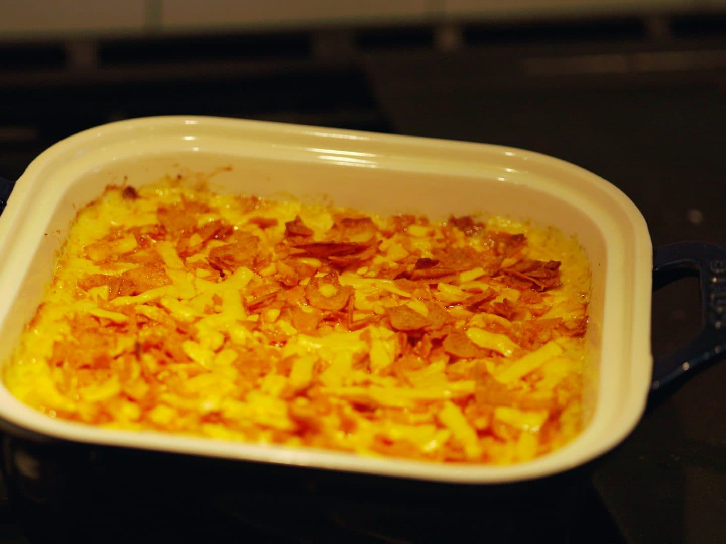 Buffalo chicken dip fresh out of the oven in a cream-and-navy baking dish, the cheddar top bubbling and golden