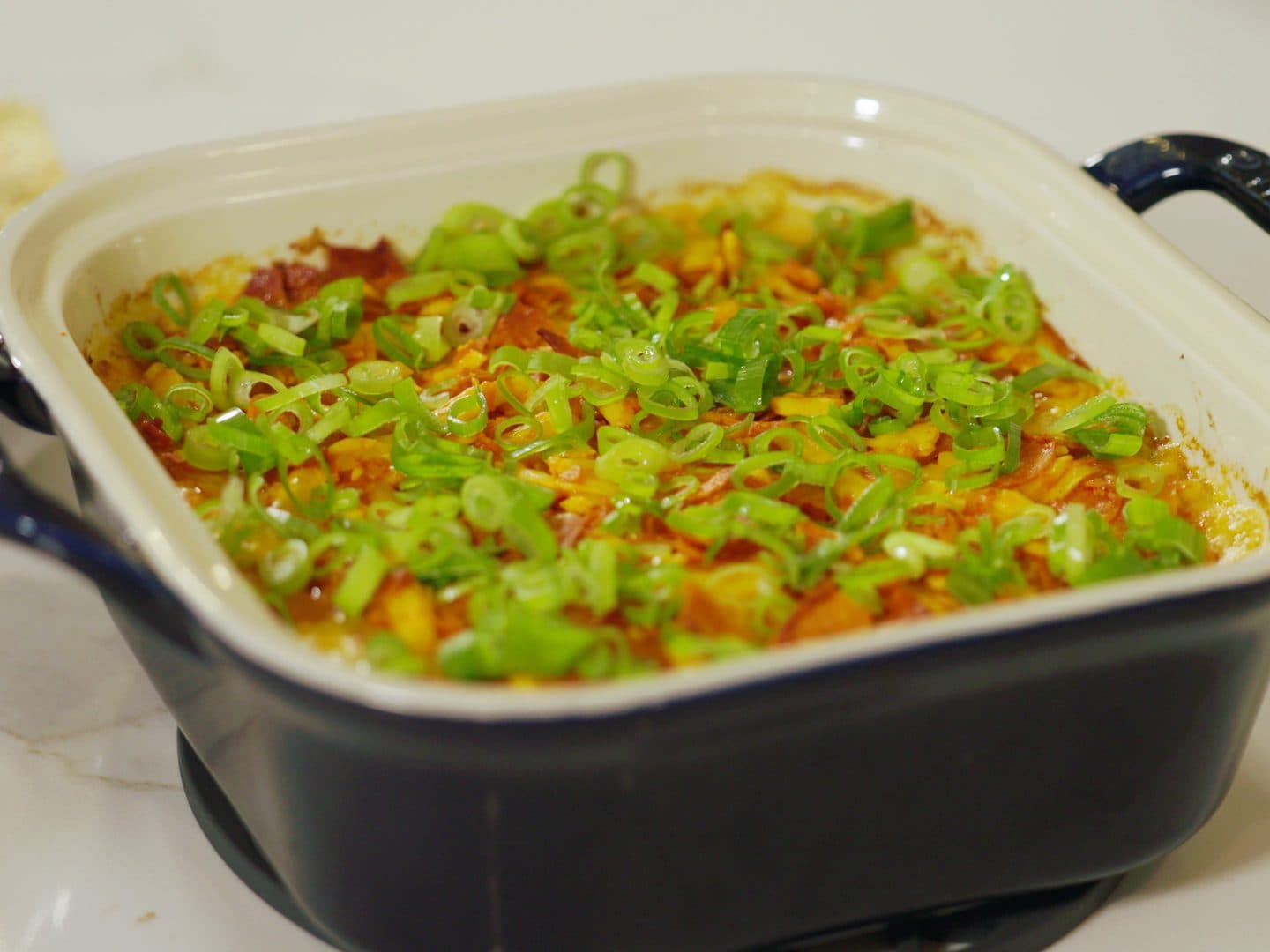 Finished buffalo chicken dip covered in thinly sliced scallions in a navy baking dish